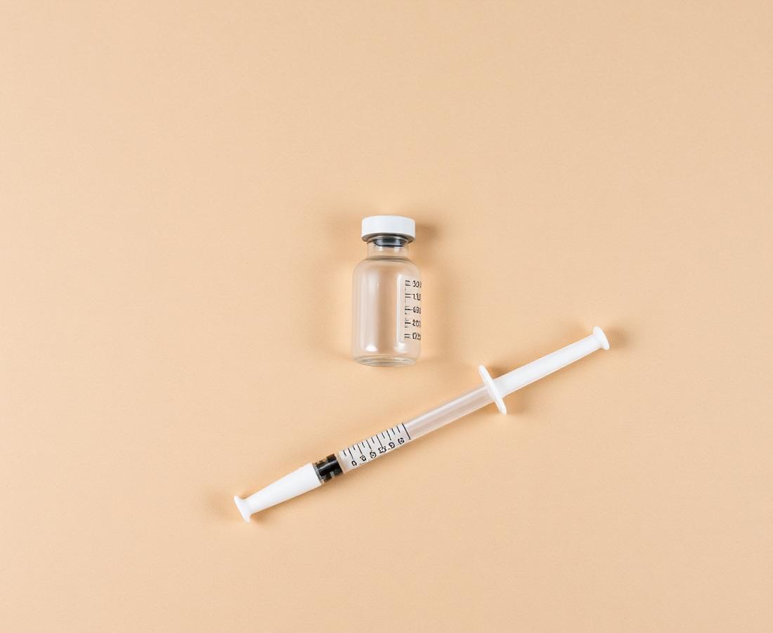 A sealed research vial beside a syringe on a warm stone surface